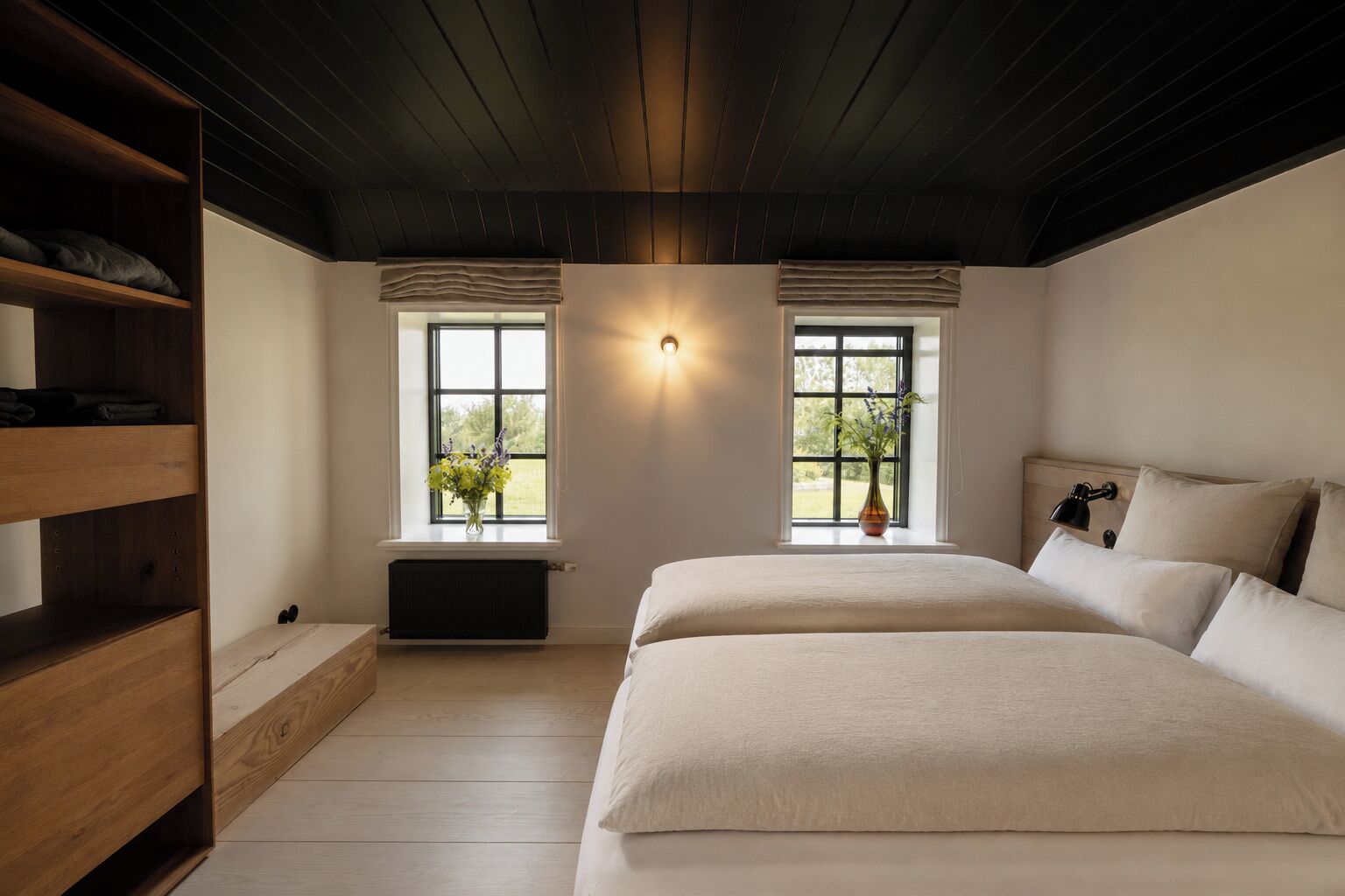 Een slaapkamer met een groot bed, twee ramen voorzien van gordijnen, een radiator en een houten plank.