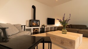 A modern living room with a wood-burning stove, a flat-screen TV, and a wooden coffee table. - Rickmer’s Hoff Cottage| Sauna, Kamin & Weitblick (Pellworm)