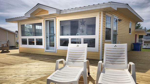 Une maison de plage avec une terrasse, deux chaises en plastique blanches et de grandes fenêtres.