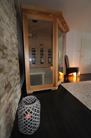 A room with a brick wall, a wooden-framed sliding door, a dark wooden floor, a white patterned rug, and a wicker basket. - Romantic cottage is looking for you! -Wi-Fi, fireplace, infrared cabin (Hellenthal)