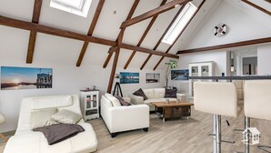 A spacious loft with exposed wooden beams, a white sofa set, a wooden coffee table, and a bar area with stools. - At the gates of Hamburg in the old country (Steinkirchen)