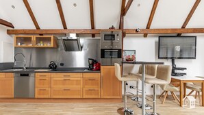A modern kitchen with wooden cabinets, stainless steel appliances, and a dining area with bar stools. - At the gates of Hamburg in the old country (Steinkirchen)