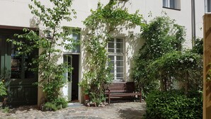 Ein Innenhof mit einem Kopfsteinpflasterweg, einer hölzernen Bank und einem Gebäude mit Fenster und Tür.