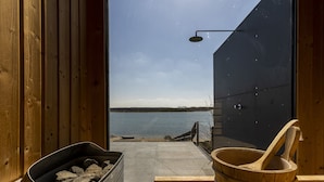 A wooden cabin with a view of a lake, a metal container with charcoal, and a wooden tub.