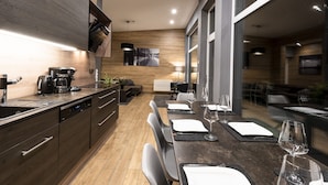 A modern kitchen with dark wood cabinetry, a central island, and a dining area with a long table set for two.