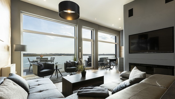 A modern living room with a large TV, comfortable seating, and a view of a body of water through large windows.