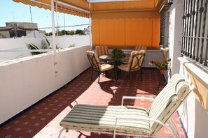 A balcony with a table and chairs, a striped lounge chair, and a potted plant.