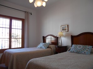 A room with two beds, a nightstand, a lamp, a picture on the wall, and a window with curtains.