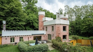 Ein schlösserähnliches Gebäude mit einem Turm, einem Schwimmbad und einem gepflegten Garten.