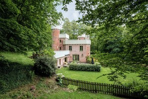 A castle-like building with a tower, surrounded by lush greenery and a wooden fence. - Castle in the woods with private SPA 45 min from Paris and Reims, 25 min Disney (Montreuil-Aux-Lions)
