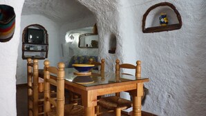 Un comedor rústico con una mesa y sillas de madera, un televisor en un estante y una pared blanca con textura.