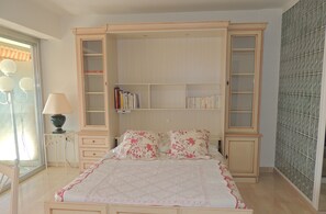 A bedroom with a bed, a nightstand, a lamp, a bookshelf, and a mirror.