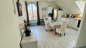 Une cuisine moderne avec un coin repas, une vue dégagée grâce à une grande fenêtre et un petit espace détente agrémenté d’un panneau indiquant « MAISON ».