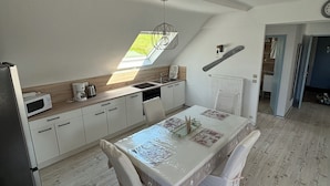 Une cuisine moderne dotée d’une verrière, de meubles blancs et d’un coin repas avec une table et des chaises.