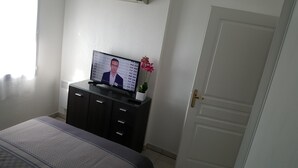Makuuhuone, jossa on sänky, lipaston päällä oleva televisio, ruukkukasvi ja ovi.