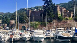 A marina with boats docked, a historic stone building in the background, and a clear blue sky.
