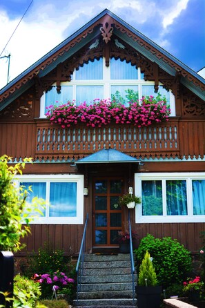 Une maison en bois avec un balcon, une porte d’entrée et des marches menant à l’entrée.