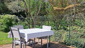Una terraza de madera con una mesa y sillas, rodeada de vegetación y una cerca de alambre.
