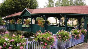 Un puente cubierto con techo verde y barandillas blancas, rodeado de flores en flor.