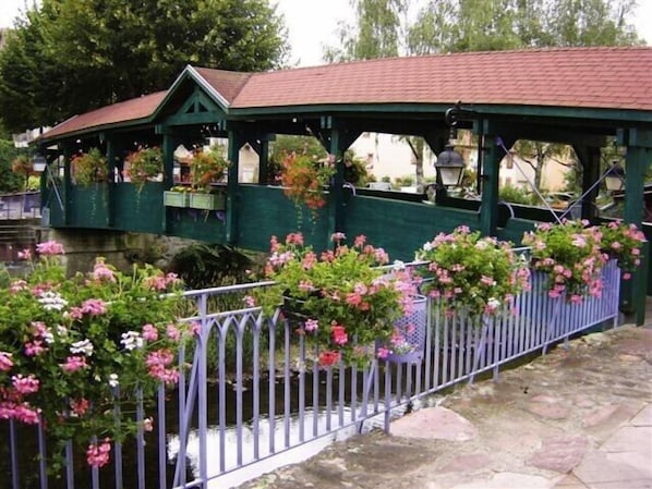 Un pont couvert avec un toit vert et des garde-corps blancs, entouré de fleurs en pleine floraison.