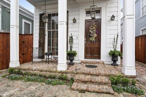 Relax on the inviting porch with two chairs and a table, surrounded by classic columns and a wooden fence.