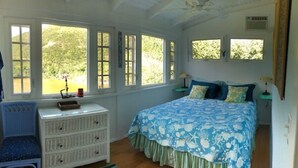 Ein Schlafzimmer mit Bett, Kommode, Stuhl und großen Fenstern.