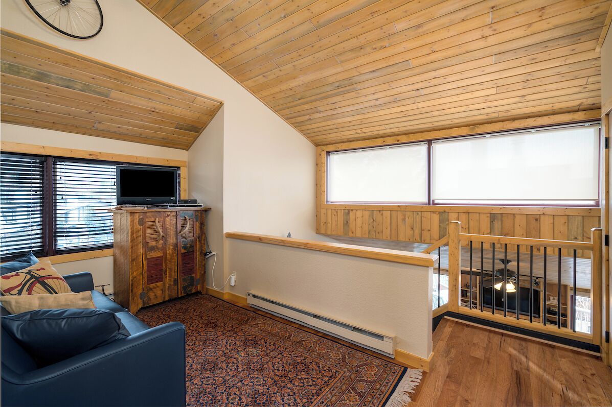 A cozy room with a wooden ceiling, a television, a cabinet, a sofa, and a window with blinds.