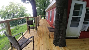 Una terraza de madera con dos sillas de mimbre y una pequeña mesa, con vistas a un paisaje verde.