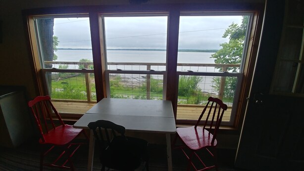Una habitación con una mesa y dos sillas, una ventana con vista a un lago y follaje.