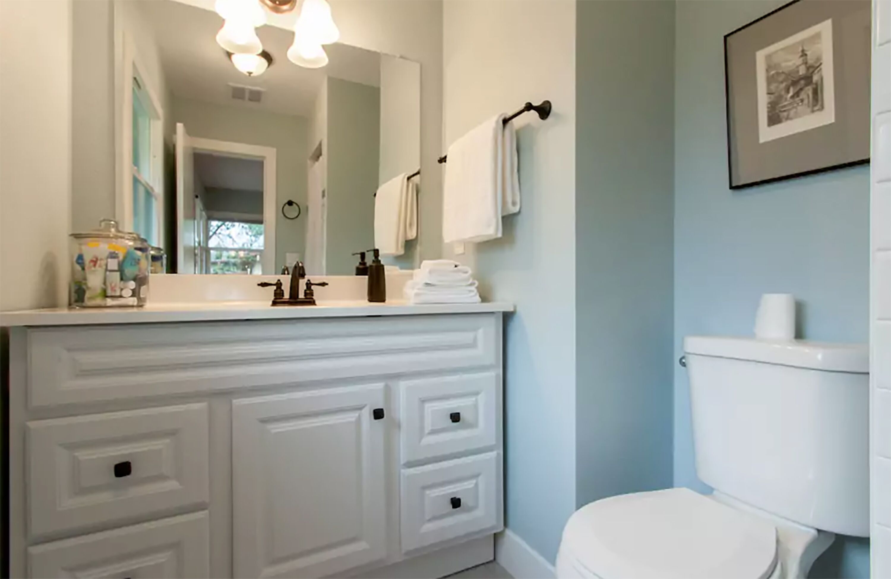 Une salle de bain avec un meuble-lavabo blanc, un grand miroir, des toilettes et un tableau encadré au mur.