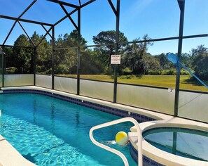 An indoor swimming pool with clear blue water, a small hot tub, and a fenced area with a sign indicating pool rules.