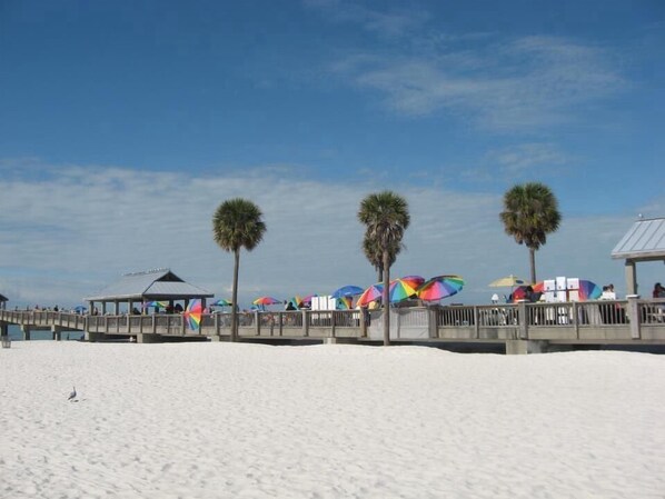 Une plage avec une promenade en bois, des palmiers et des parasols colorés.