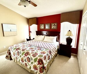 A bedroom with a bed, a nightstand, a lamp, a ceiling fan, and a window with blinds.