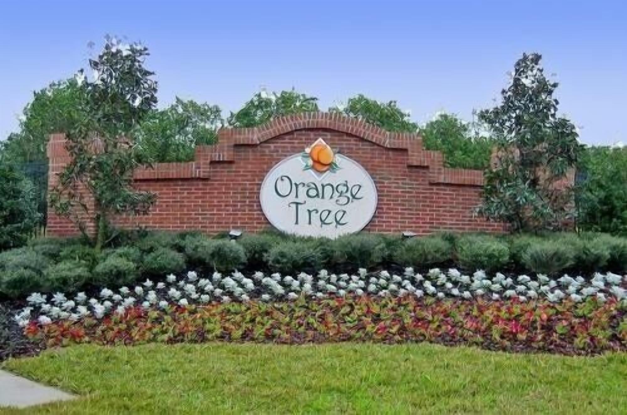 Schild für 'Orange Tree' mit einer Ziegelwand und einem Garten davor.