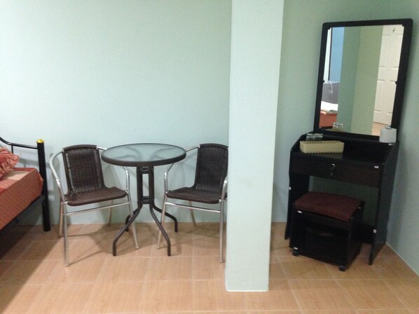 A small room with a bed, a round table with two chairs, a mirror, and a small cabinet.