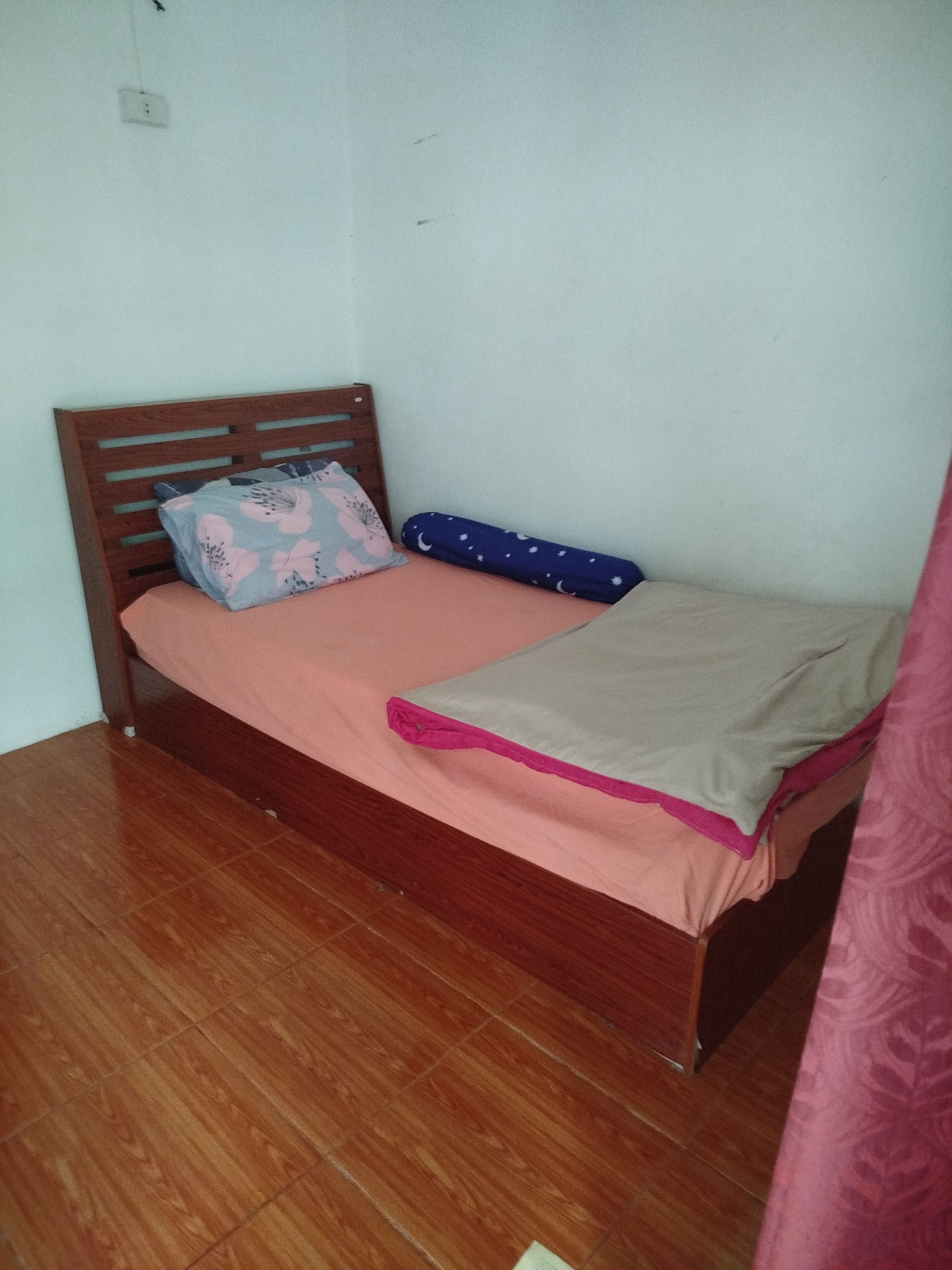 Una cama individual con estructura de madera, un colchón rosa y dos almohadas.