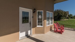 Una casa de color crema con una puerta blanca y un porche pequeño con sillas Adirondack rojas.