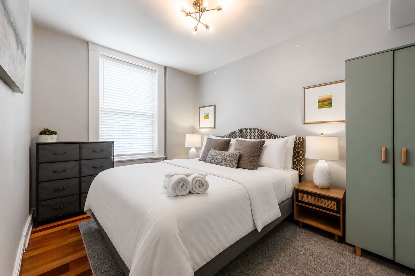 A modern bedroom with a large bed, bedside lamps, a dresser, and a wardrobe.