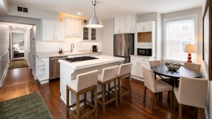 Una cocina moderna con armarios blancos, una isla central con taburetes, electrodomésticos de acero inoxidable y un comedor con una mesa redonda y sillas.