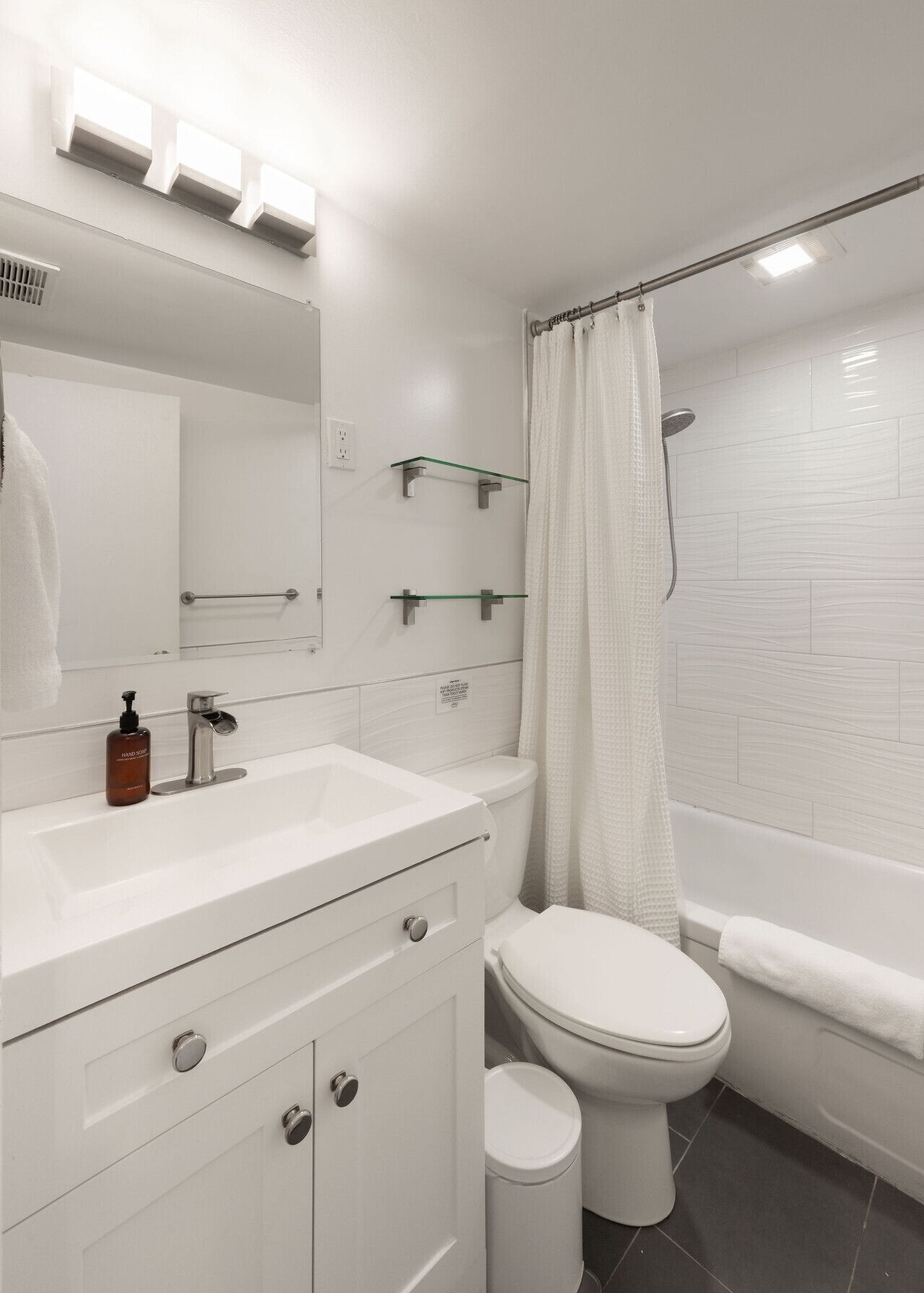 A modern bathroom with a white sink, mirror, toilet, and bathtub.