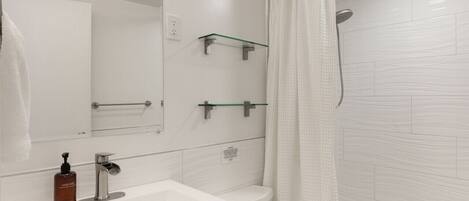 A modern bathroom with a white sink, mirror, toilet, and bathtub.