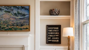 Una habitación con un sillón color crema, una lámpara, un cartel enmarcado y un cuadro en la pared.