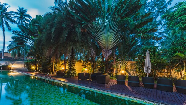A swimming pool with tiled flooring, surrounded by palm trees and lounge chairs. - Condo in Bangtao in Kris Condo - Unit402 (Choeng Thale)