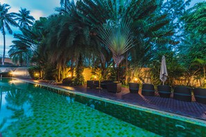 Una piscina con pavimento piastrellato, circondata da palme e lettini da relax.