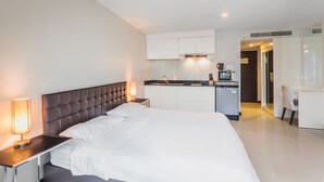 A modern hotel room with a large bed, bedside table, lamp, and a kitchenette area with a coffee machine and microwave. - Condo in Bangtao in Kris Condo - Unit402 (Choeng Thale)