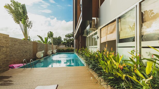 A modern outdoor pool area with a wooden deck, lounge chairs, and tropical plants. - Condo in Karon in Chic Condo - Unit A108 (Karon)