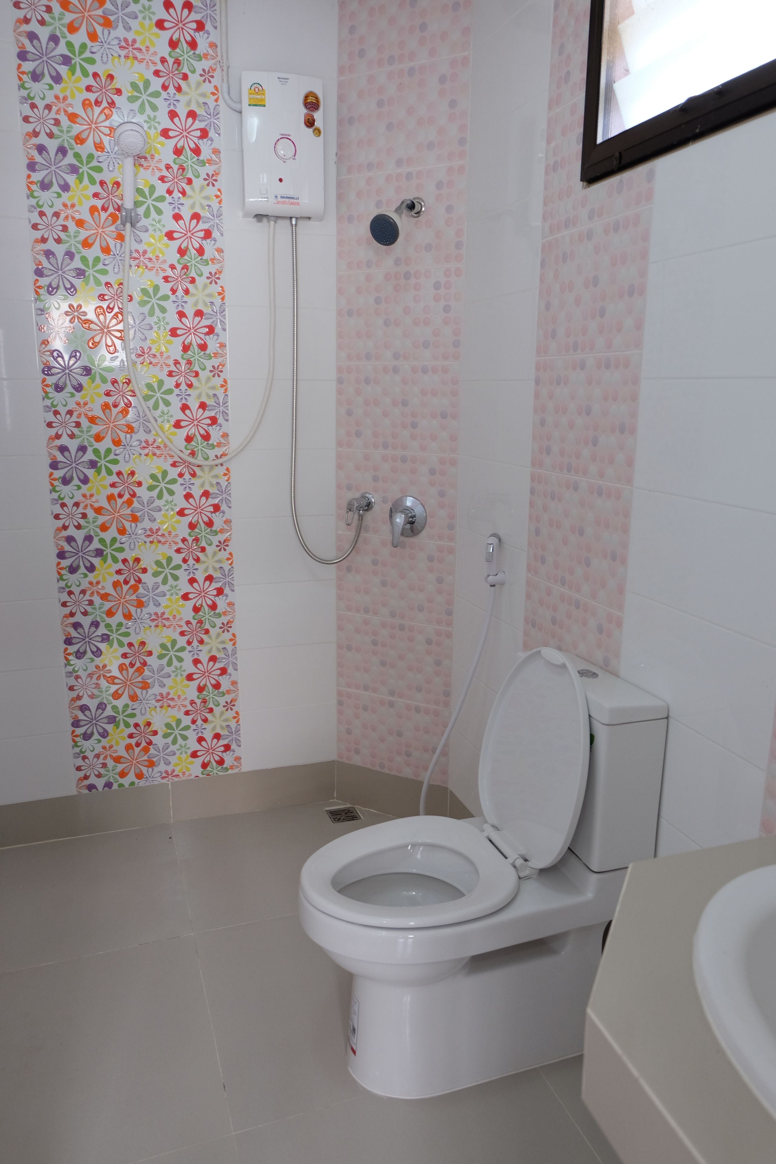 A bathroom with a toilet, shower, and a colorful floral shower curtain.