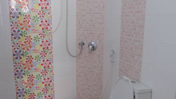 A bathroom with a toilet, shower, and a colorful floral shower curtain.