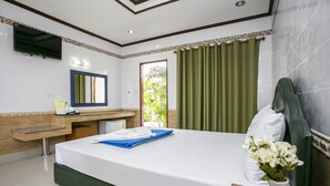 Quarto de hotel com cama, escrivaninha com cadeira, espelho, televisão e janela com cortinas.