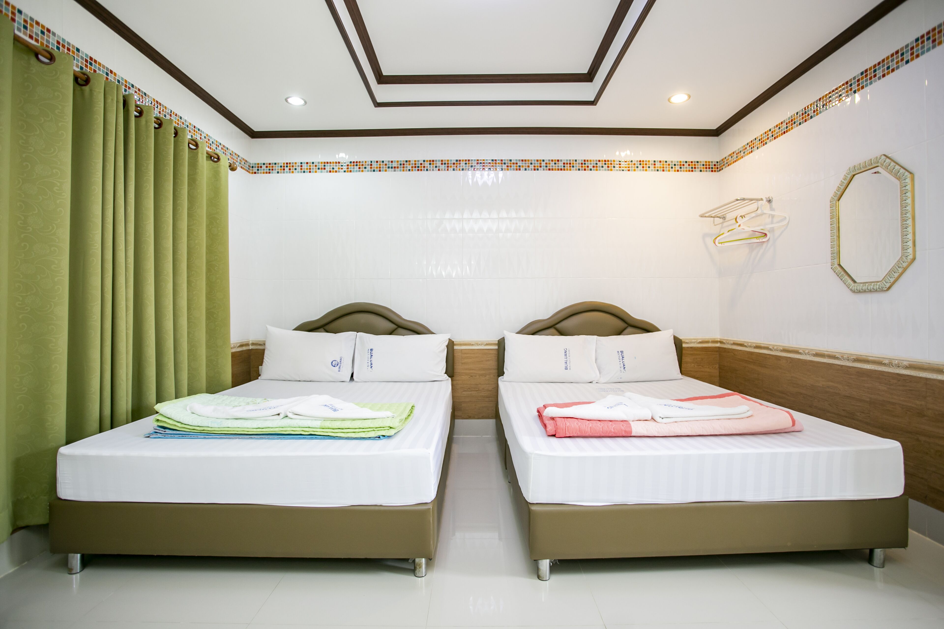 A hotel room with two beds, a green curtain, a tiled ceiling, and a mirror on the wall.